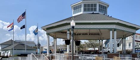 A gazebo with a central dome and a surrounding railing, located in a public space with flags and benches.