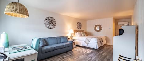 A compact living space with a sofa, a bed, a dining area with a table, and a hanging light fixture.