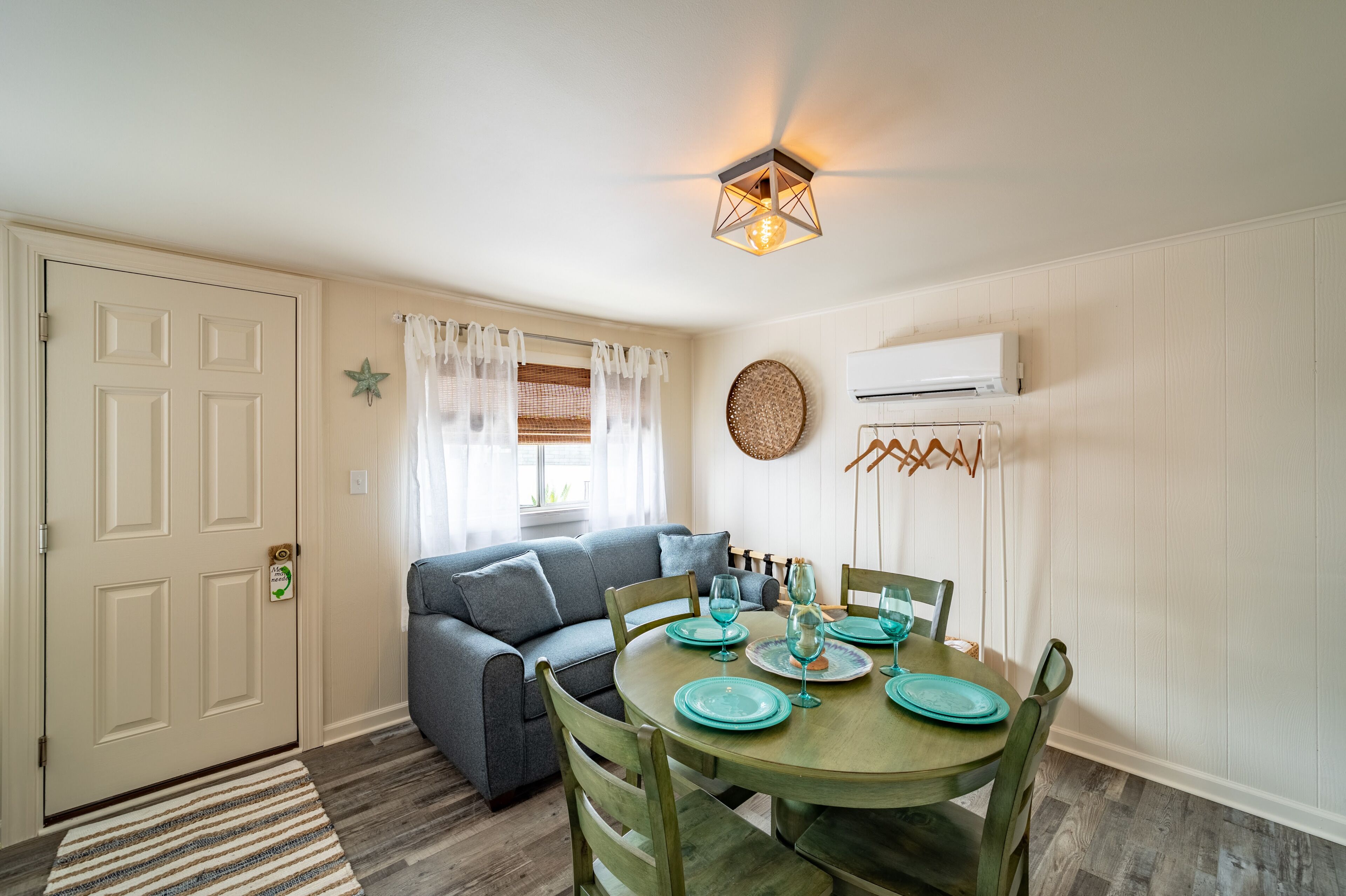 A dining area with a round table set for four, a grey sofa, and a ceiling light fixture.