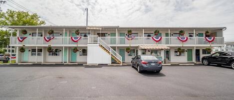 A two-story motel with a central staircase, a covered front porch, and a car parked in front.