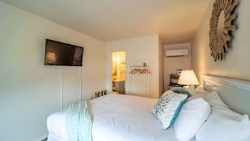 Habitación de hotel con cama, televisor de pantalla plana montado en la pared, equipo de aire acondicionado y un adorno mural.