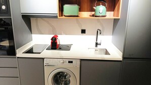 Pieni, käytännöllinen keittiö, jossa on pesukone, pesuallas, vedenkeitin ja mikroaaltouuni.