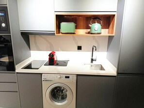 A compact kitchen with a washing machine, a sink, a kettle, and a microwave. - Luxury Stay in Maârif: High-Speed WiFi & Free Parking (Dar-el-Beida)