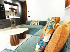 A modern living room with a sofa, a coffee table, and a washing machine in the background. - Luxury Stay in Maârif: High-Speed WiFi & Free Parking (Dar-el-Beida)