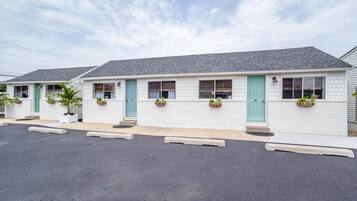 Una hilera de edificios de motel de una planta con fachadas blancas y puertas color turquesa, cada uno con un pequeño porche y macetas.