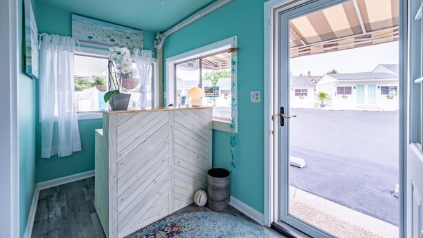Ein Zimmer mit türkisfarbenen Wänden, einem Deckenventilator, einem Fenster mit Blick auf die Straße und einer zur Außenseite führenden Tür.