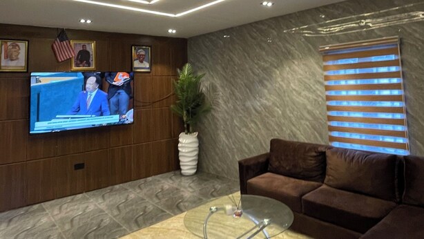Una sala de estar moderna con un televisor de pantalla plana, una mesa de centro de vidrio, un sofá marrón y una planta decorativa.