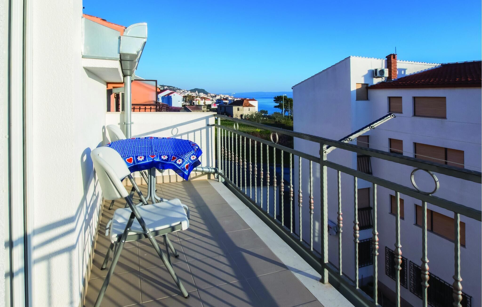 A balcony with a table and chairs, a railing, and a view of the sea and buildings.