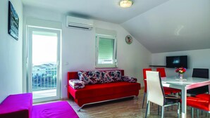 Ein modernes Wohnzimmer mit einem roten Sofa, einem Esstisch mit roten Stühlen, einem Fernseher und einem Balkon mit Blick.