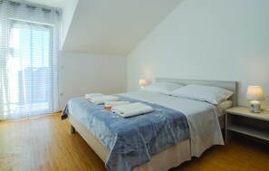 A bedroom with a bed, two bedside tables, a window with curtains, and a lamp on each table.