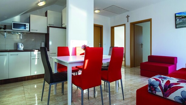 Eine moderne Küche mit Mikrowelle, ein Essbereich mit weißem Tisch und roten Stühlen sowie ein rotes Sofa.