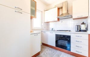 A modern kitchen with white cabinets, a stainless steel range hood, a built-in oven, and a coffee maker. - Apartment in Podstrana (256) (Podstrana)