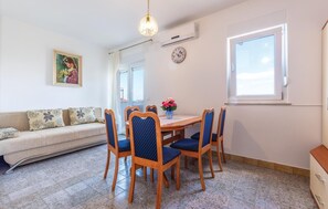A dining area with a round wooden table, blue upholstered chairs, a vase of flowers, a clock, and a painting on the wall. - Apartment in Podstrana (256) (Podstrana)