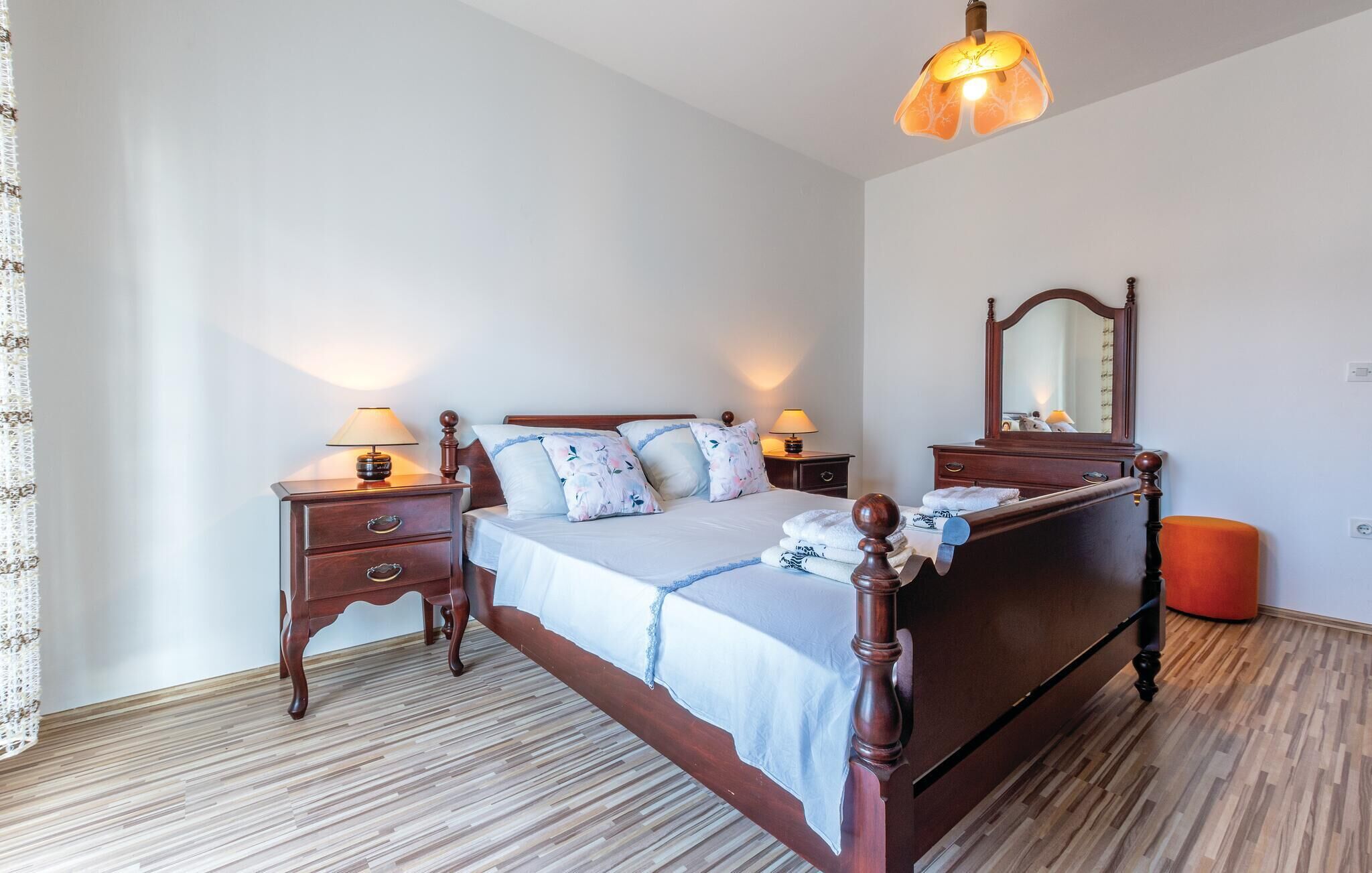 A bedroom with a wooden four-poster bed, two bedside tables with lamps, a mirror, and a wooden floor.