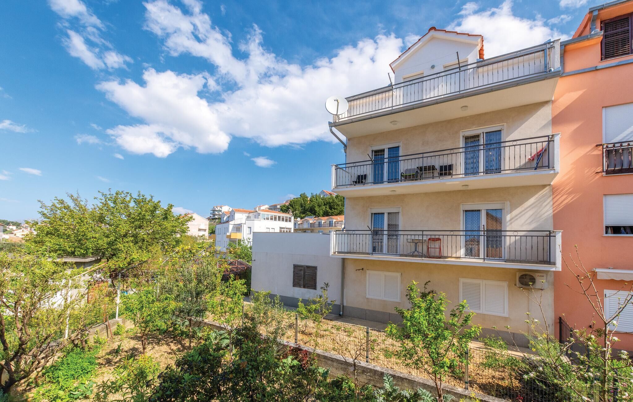 A multi-story residential building with balconies, a clear sky, and surrounding greenery.