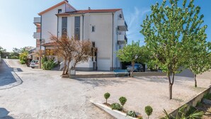 Un immeuble à plusieurs étages, doté d’un toit recouvert de tuiles, d’une allée et d’un petit espace de stationnement.