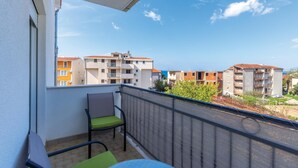 Un balcon avec une chaise et une table, donnant sur une rangée d’immeubles à plusieurs étages, chacun doté d’un balcon.