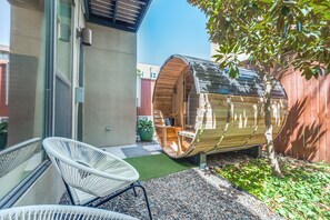 A modern building with a glass door, a wooden structure with a curved roof, and a small garden area with a tree and a white chair. - The Q: Dallas - Spacious 3 bedroom Dallas townhome w. Rooftop Sauna Gym DT (Dallas)