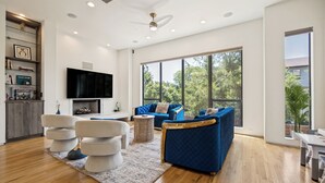 Ein geräumiges Wohnzimmer mit großem Fernseher, blauen Sofas, einem Kamin und einem Essbereich.