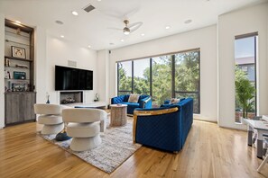Ein geräumiges Wohnzimmer mit großem Fernseher, blauen Sofas, einem Kamin und einem Essbereich.