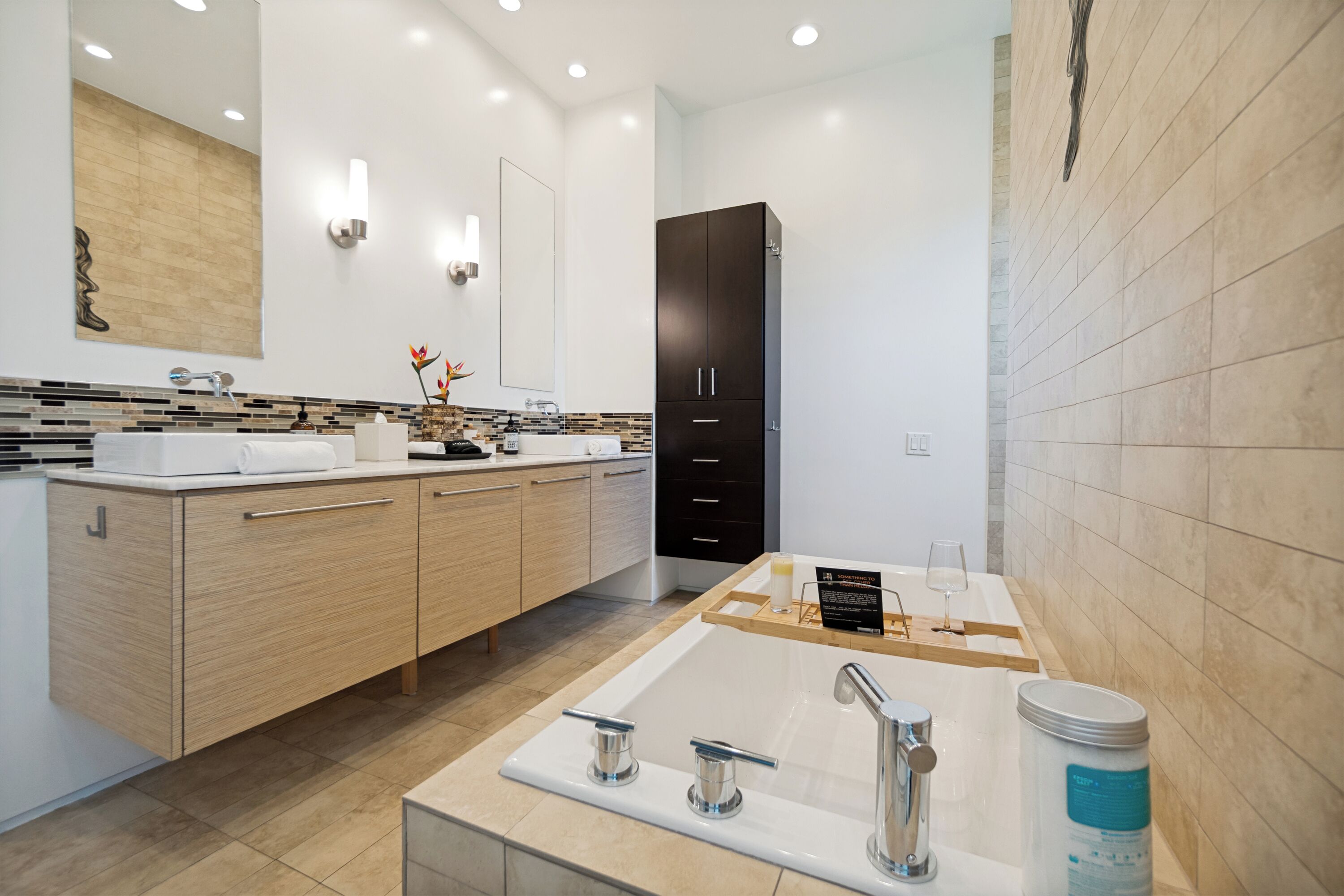A modern bathroom with a large sink, two faucets, a mirror, and a cabinet.