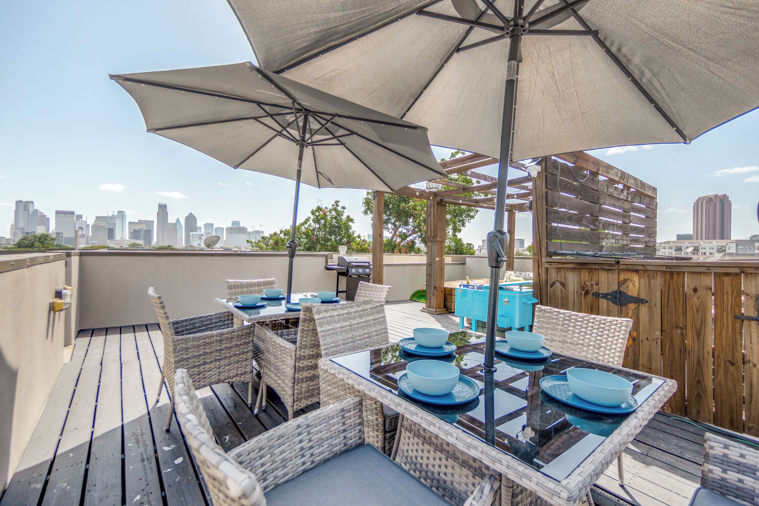 Une terrasse extérieure avec des meubles en osier, une table dressée avec des bols bleus, et une vue sur les gratte-ciel de la ville en arrière-plan.