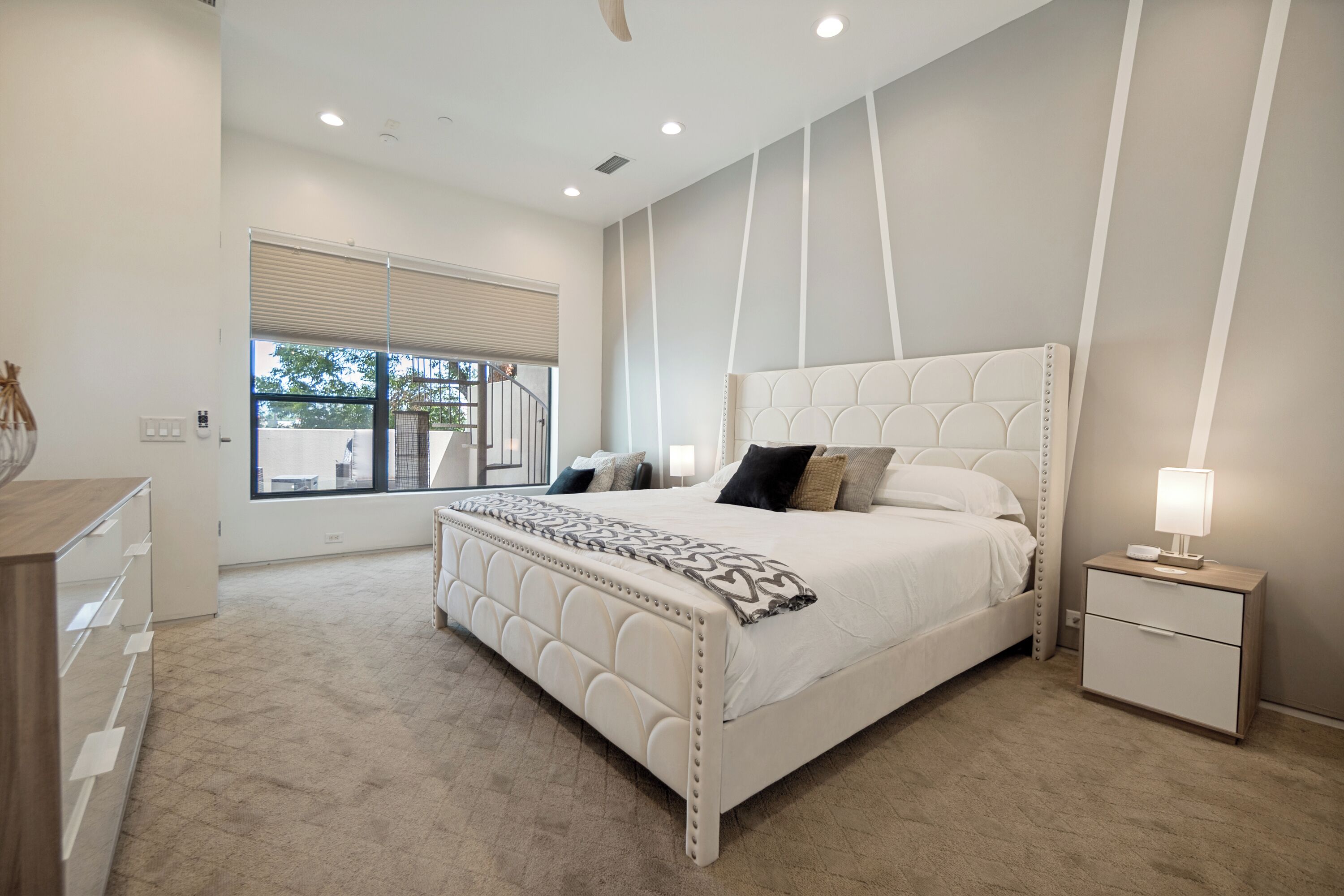 Une chambre à coucher avec un grand lit, une table de chevet, une lampe et une fenêtre avec des stores.