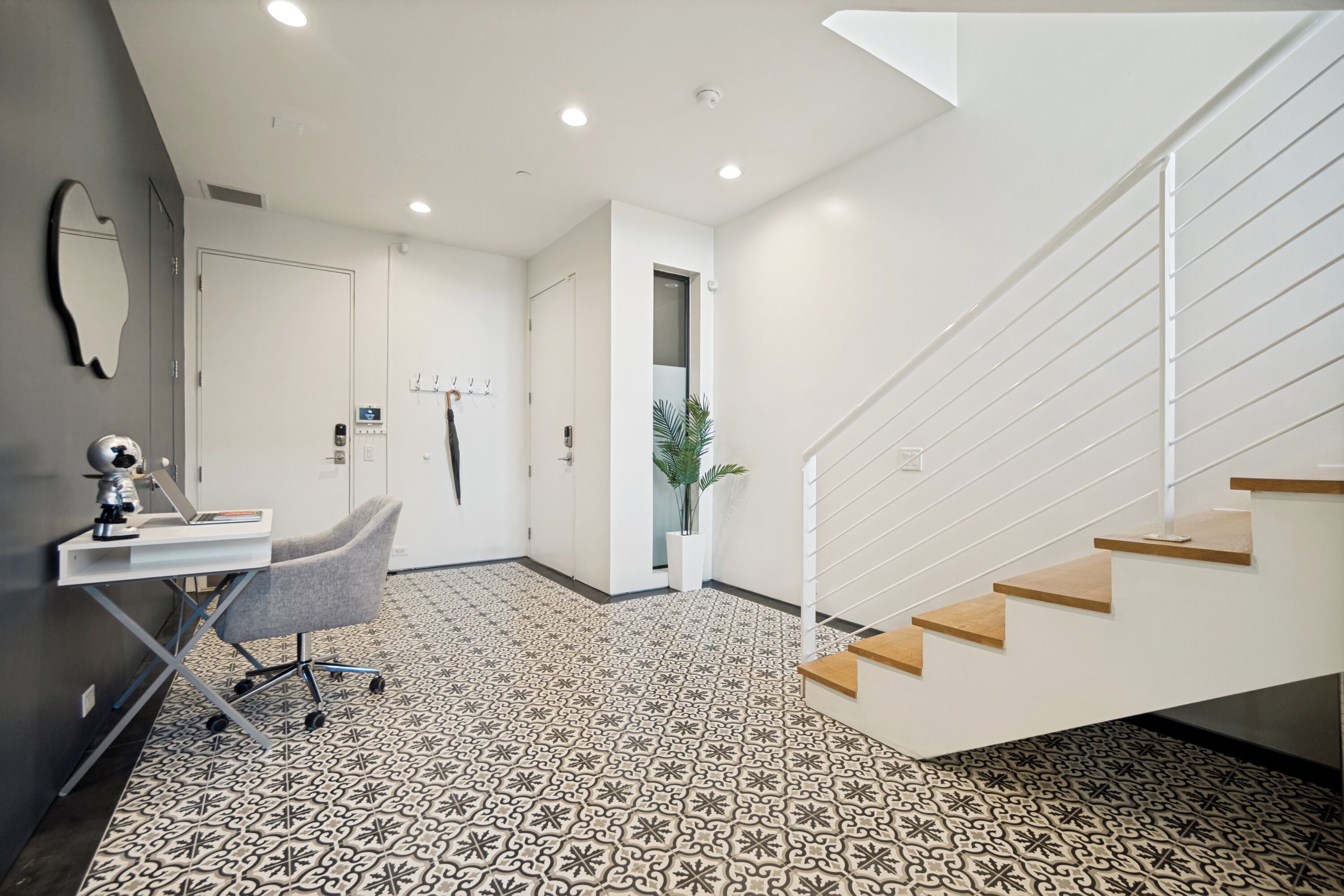 A modern interior with a staircase, a desk with a chair, and patterned flooring.
