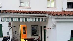 A white building with a tiled roof, a covered patio with a table and chairs, a hanging chair, and a grill. - Villa la Mina (Gijón)