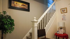Eine Treppe mit weißen Geländern, ein gerahmtes Bild an der Wand, ein Blumentopf, ein Stuhl und ein kleiner Tisch mit roter Decke.