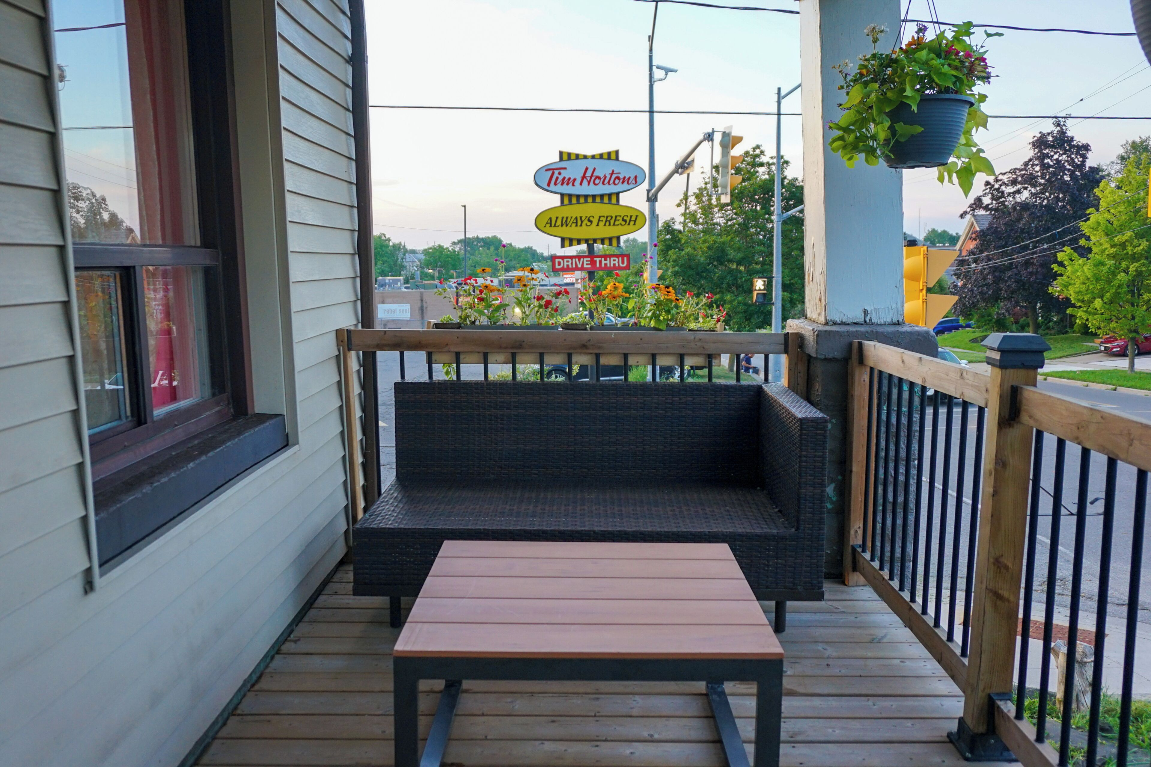 A porch with a wooden bench, a Tim Hortons sign, and a hanging planter.