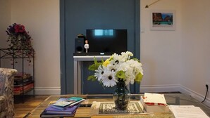 A living room with a flat-screen TV on a stand, a vase with flowers on a table, and a framed picture on the wall.