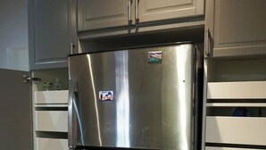 A stainless steel refrigerator with a two-door design, located in a kitchen with wooden flooring and white cabinetry.