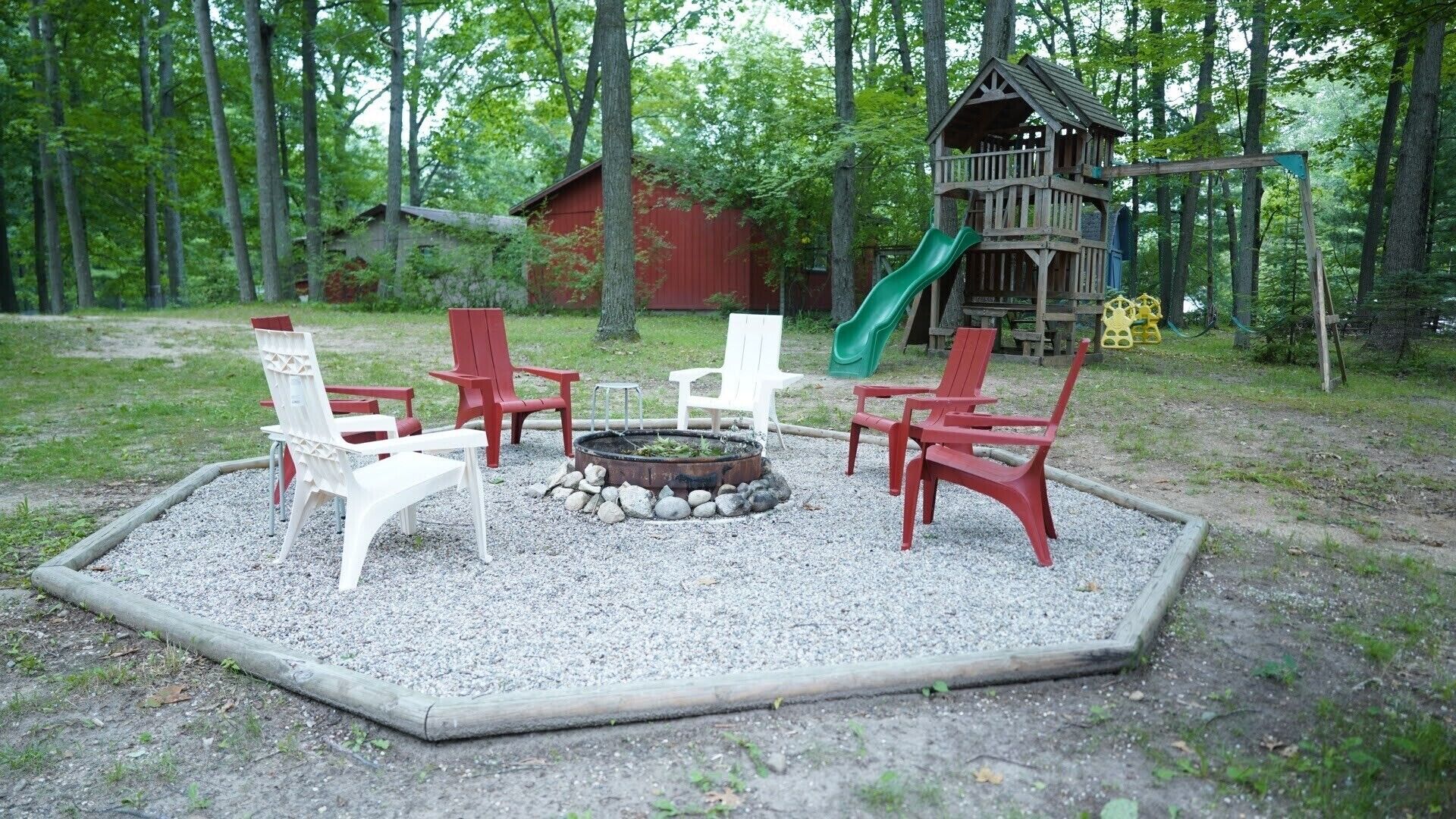 A playground with a fire pit, red and white chairs, and a wooden playhouse with a slide.
