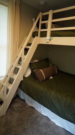Un letto a castello con una scala in legno, una coperta verde e un cuscino marrone.