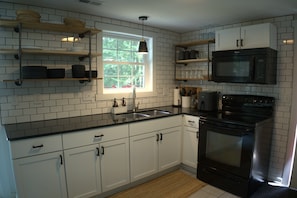 A kitchen with white cabinets, a black stove, and a window with a view of greenery. - Big Blue at Little Long Lake (Harrison)