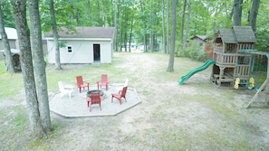 A backyard with a fire pit, outdoor seating, a wooden playhouse, and a slide. - Big Blue at Little Long Lake (Harrison)
