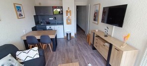 Ein kompakter Wohnbereich mit Küchenzeile, Essplatz und Wand-Fernseher.