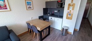 A compact living space with a kitchenette, a dining area with a table and chairs, and a small trash bin. - Le nid des 2 Alpes - Pied de pistes - Hypercentre (Les Deux Alpes)