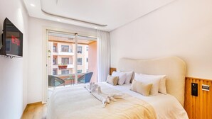 Habitación de hotel con cama, televisor, balcón y vista a edificios, además de un panel de pared de madera.