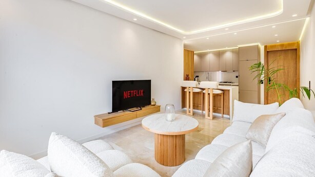 Una sala de estar moderna con un televisor de pantalla plana, una mesa de centro redonda de madera y un sofá.