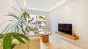 Una sala de estar moderna con un televisor de pantalla plana, un sofá, una mesa de centro y ventanas amplias.