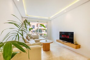 A modern living room with a flat-screen TV, a sofa, a coffee table, and large windows. - Stunning apartment with a terrace in Gueliz-Majorelle (Marrakech)