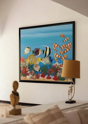 A framed painting of an underwater scene with fish and coral, a lamp, and a small wooden figure on a table. - Luxury Family Villa on Yalku Lagoon · Private Cenote · Akumal (Tulum)