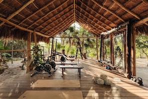 Un espace extérieur abrité, doté d’un plancher en bois, d’équipements de musculation et d’un toit de chaume.