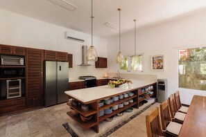 Une cuisine moderne dotée d’appareils électroménagers intégrés, un îlot central agrémenté d’un panier de fruits et un coin repas avec des chaises en bois.