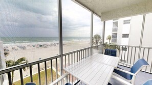 A balcony with a white table and blue chairs, overlooking a beach with umbrellas and people. - Crescent Arms 304S Siesta Key Florida (Sarasota)