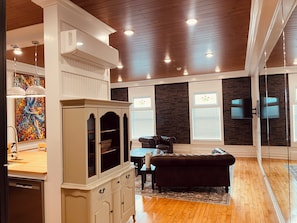 A spacious living room with a wooden floor, a black leather sofa, a white cabinet, and a painting on the wall.