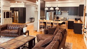 Un'ampia zona giorno con un divano in pelle marrone, un tavolino da caffè e un'area pranzo con sedie di legno, con una cucina sullo sfondo.