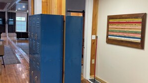 Un corridoio con pannelli in legno, armadietti blu e una mopa appoggiata al muro.